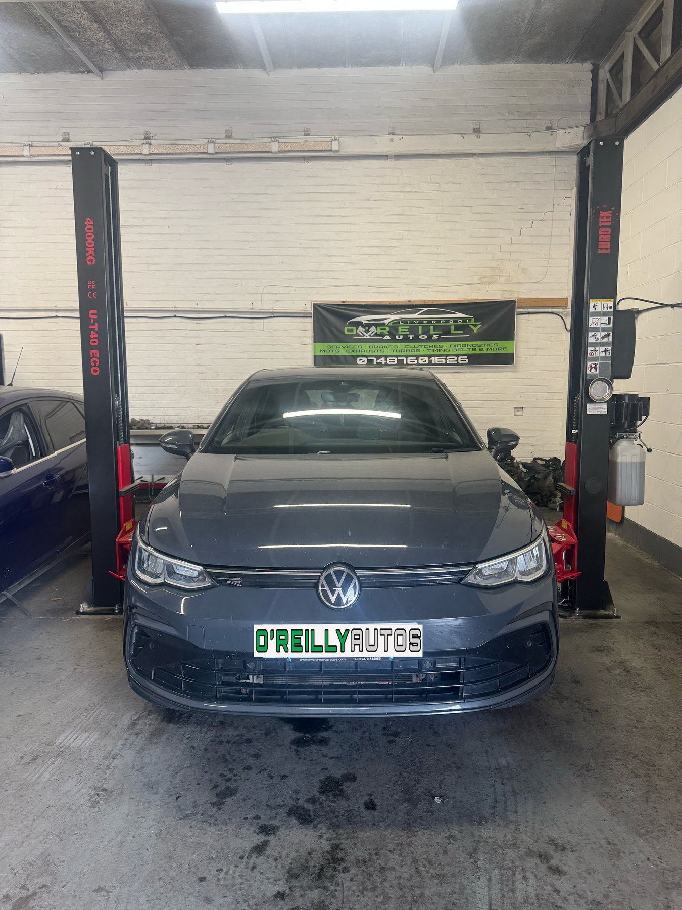 A grey Volkswagen Golf on the two-post ramp under the O'Reilly Autos banner