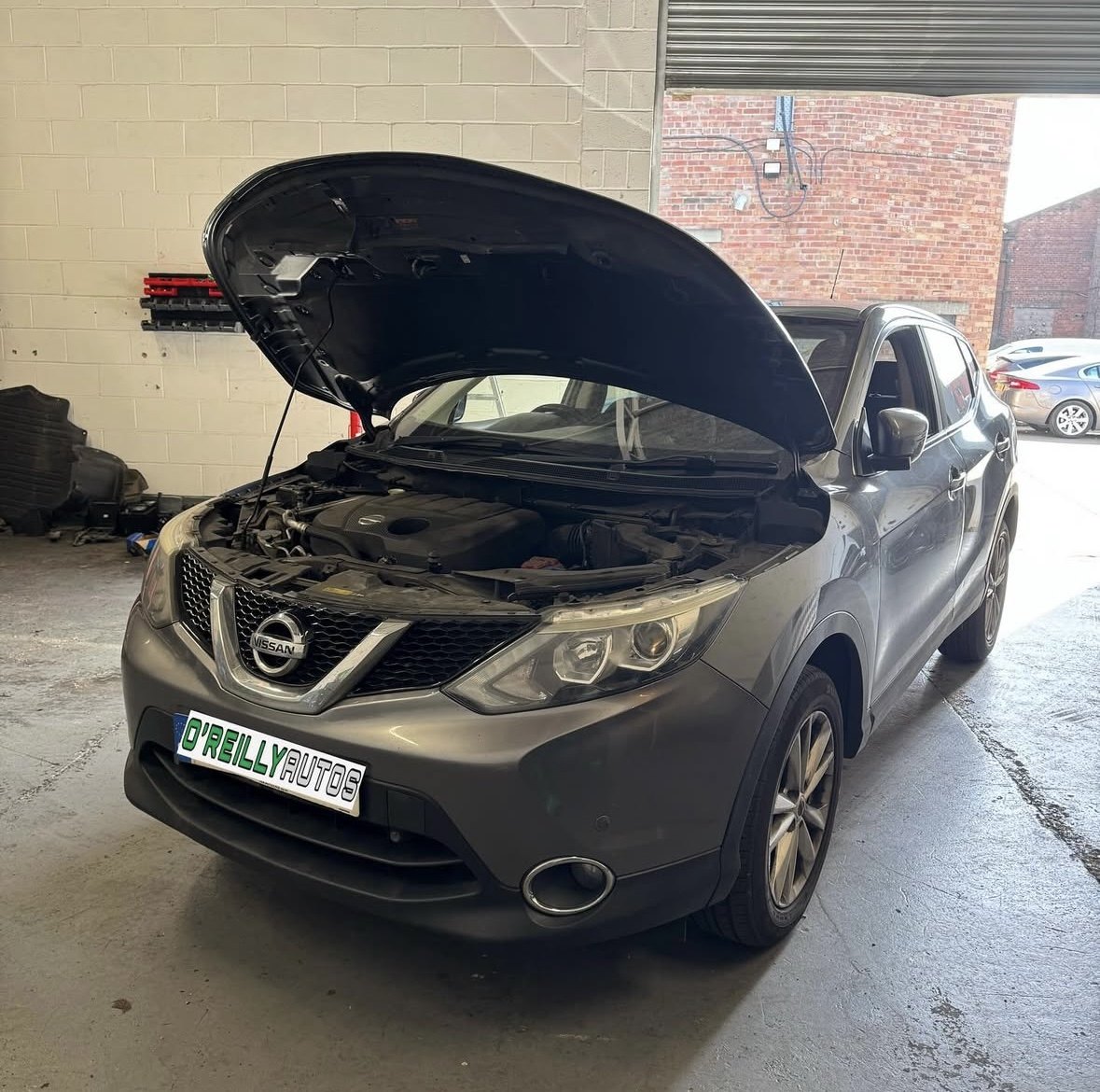 A grey Nissan Qashqai with its bonnet up by the open workshop door
