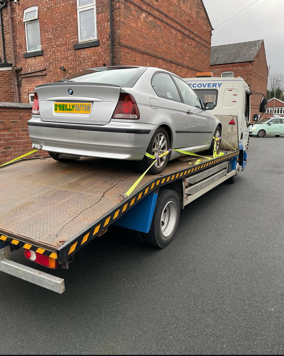A silver BMW strapped to a recovery truck on the street outside