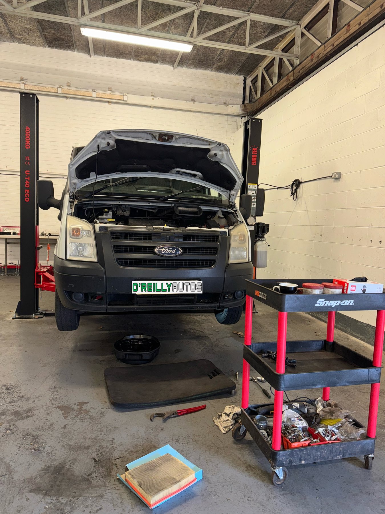 A Ford Transit with its bonnet up and a red tool trolley in front of it